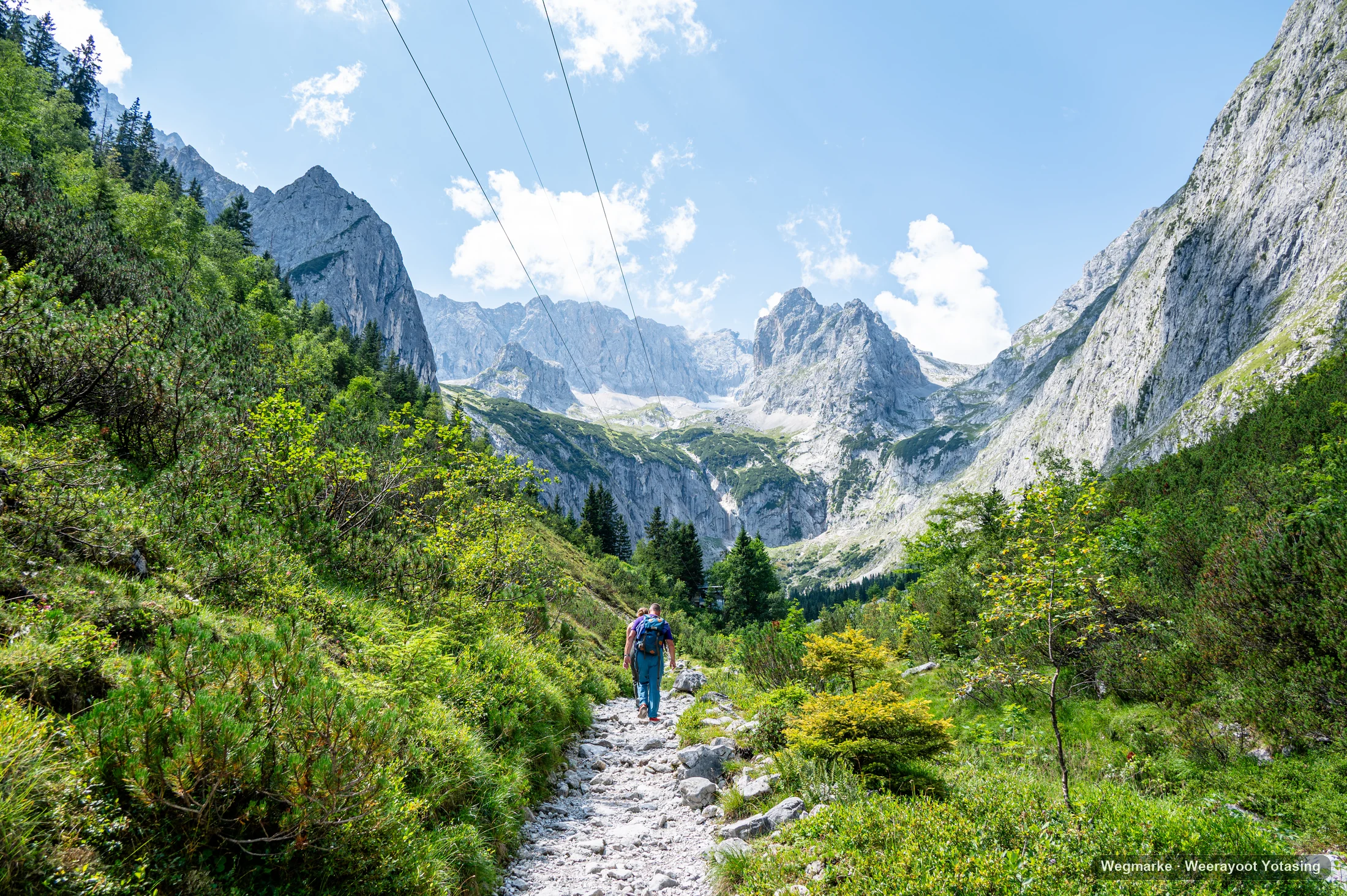 A hiker follows a rocky path toward a wall of alpine peaks