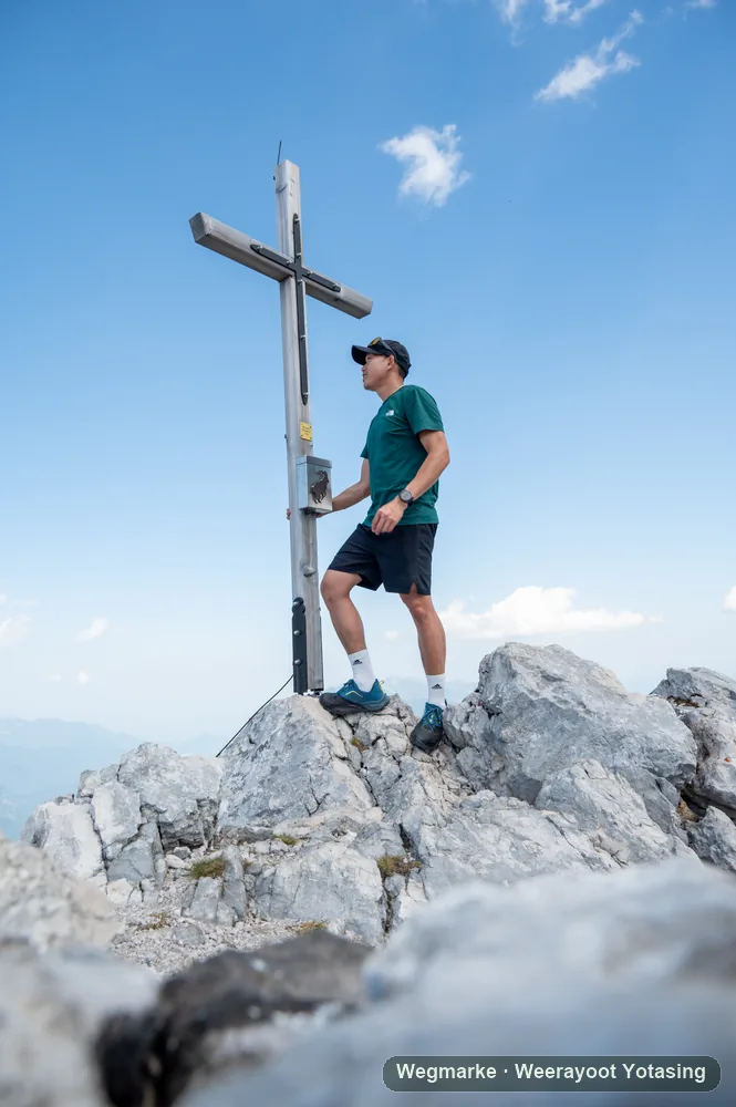 A hiker standing beside a summit marker